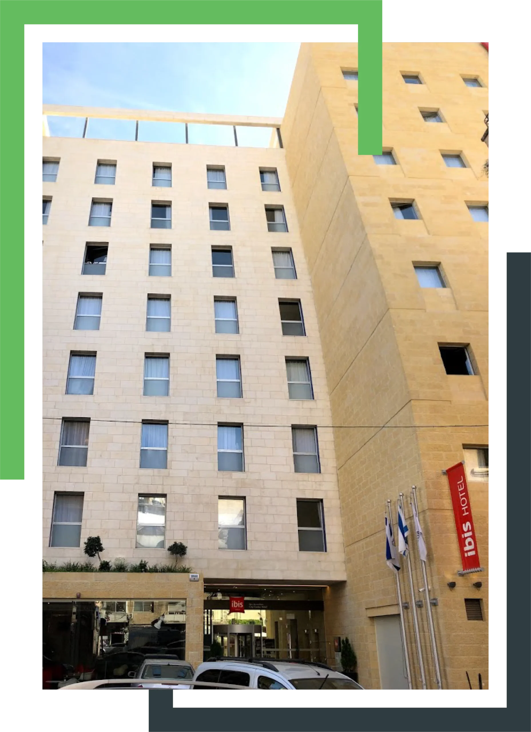 בניין מלון בגוון בהיר עם חלונות מלבניים, דגלים בכניסה ושלט אדום עם הכיתוב "ibis hotel."