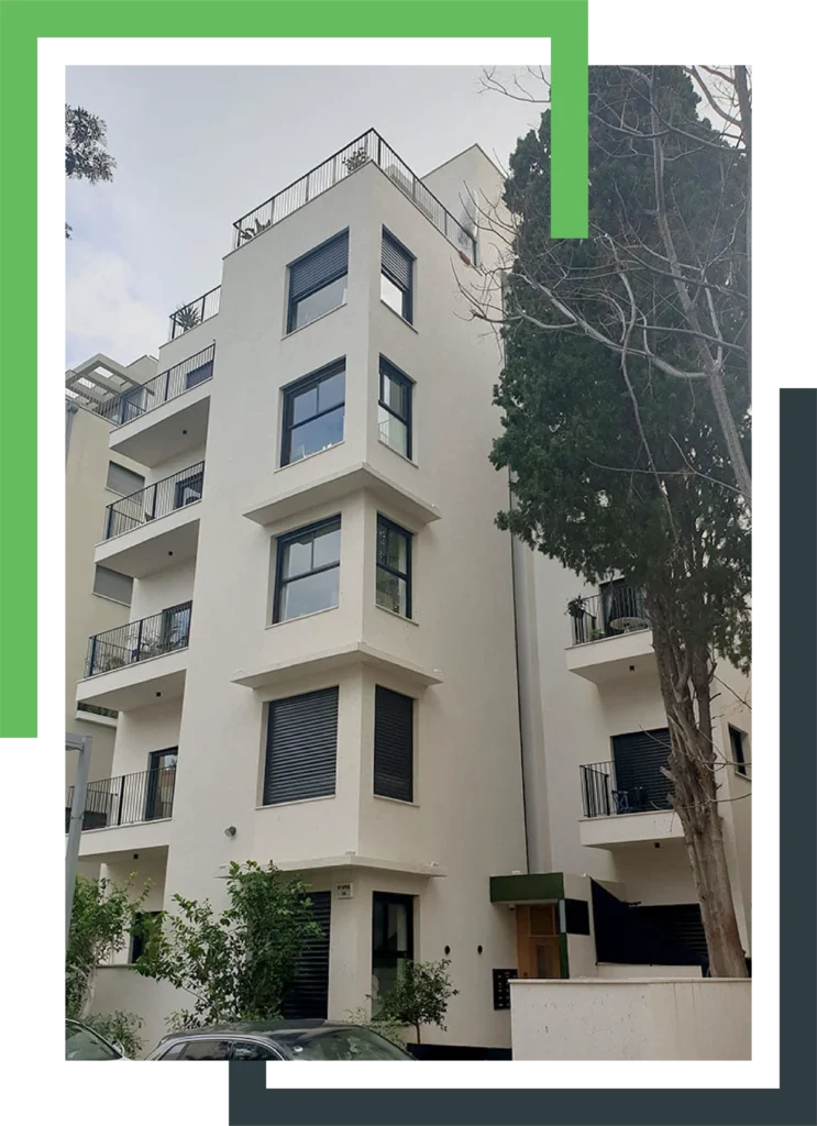 בניין מגורים בעל עיצוב מודרני עם חלונות גדולים ומרפסות עם מעקות ברזל, מוקף בצמחייה ועצים.
